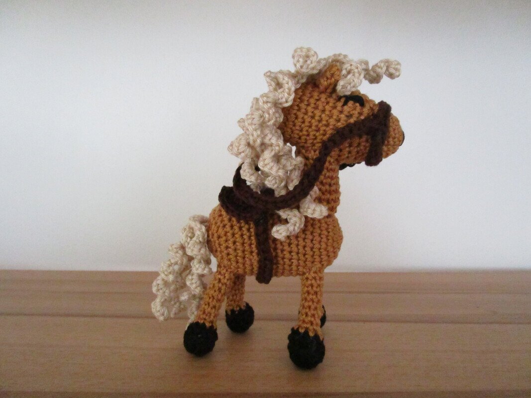Seitenansicht eines gehäkelten Amigurumi-Pferdes mit krauser cremefarbener Mähne