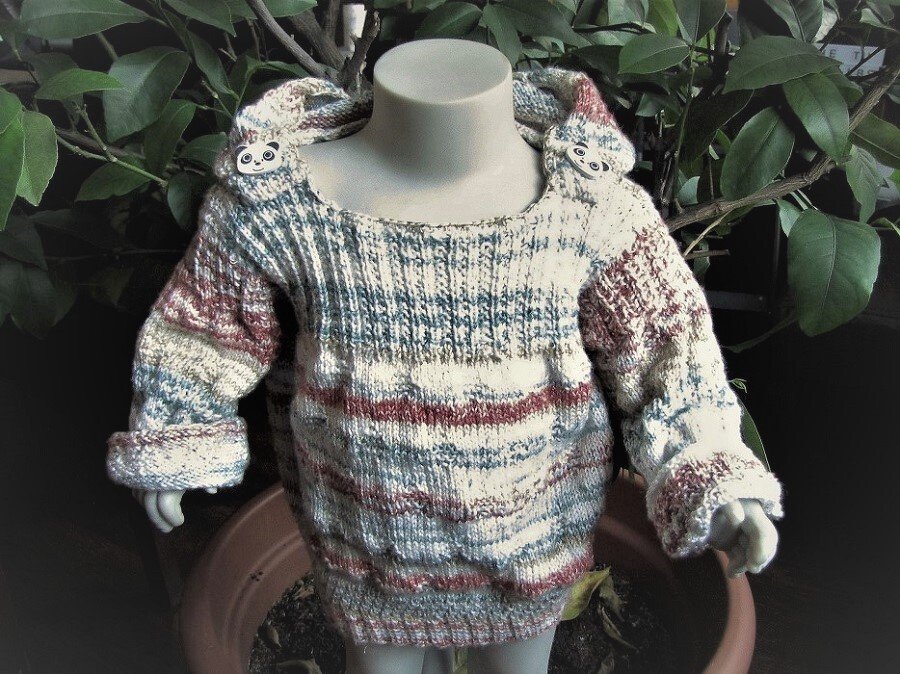 Mehrfarbiger gestrickter Kinderpullover mit Tierknöpfen auf einer Kinderpuppe