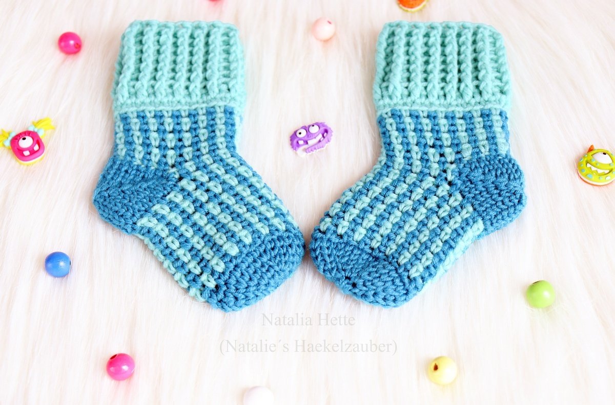 Mint and blue crocheted baby socks with a checkered stitch pattern and ribbed cuffs on a white background.
