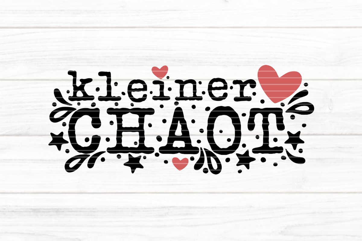 Schwarzer Schriftzug ‚kleiner CHAOT‘ mit roten Herzen, Sternen und Punktornamenten auf hellem Holzplanken-Hintergrund