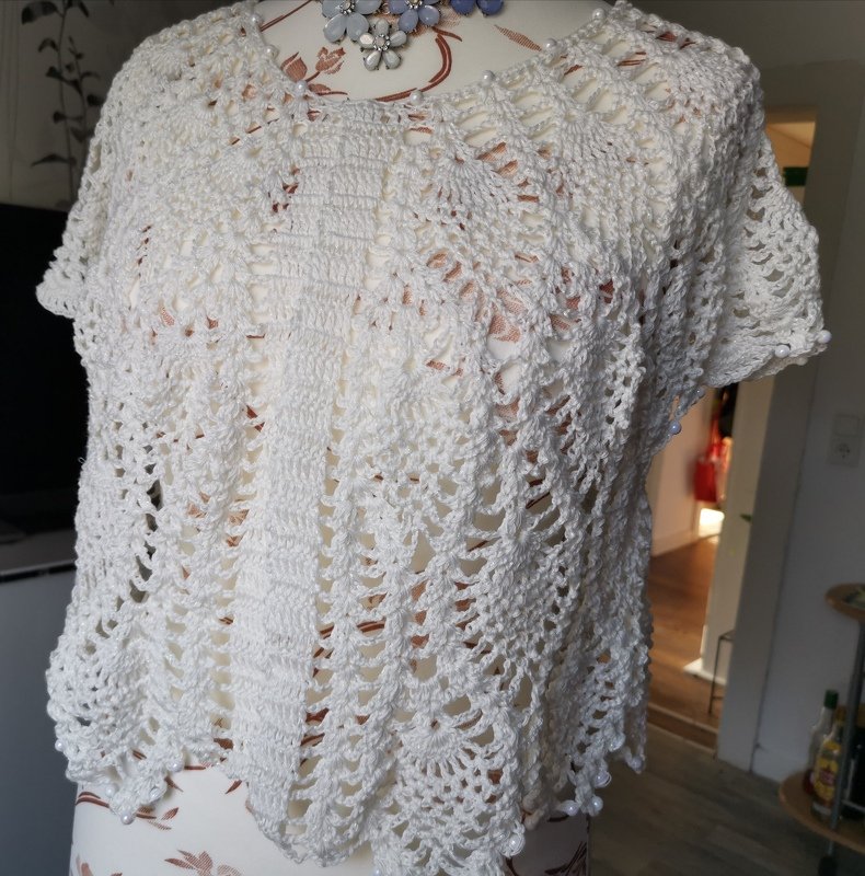 Weißer gehäkelter Bolero mit offenem Muster, kurzen Ärmeln und Perlenverzierung auf einer Schneiderpuppe.