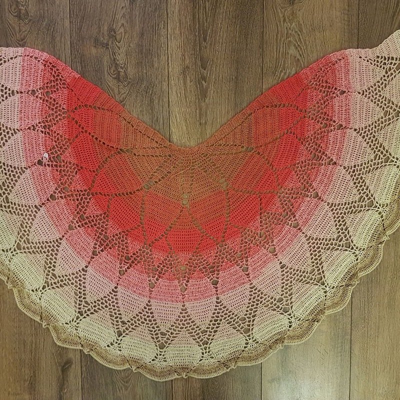 Halbrundes gehäkeltes Tuch mit Farbverlauf von Koralle zu Beige und Spitzenmuster auf Holz.
