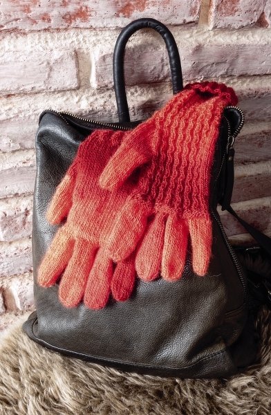 Rot-orange gestrickte Fingerhandschuhe auf schwarzem Rucksack