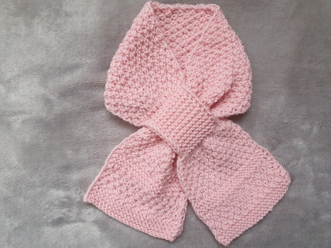 Gestrickter rosa Babyschal mit Durchziehschlaufe auf grauem Hintergrund
