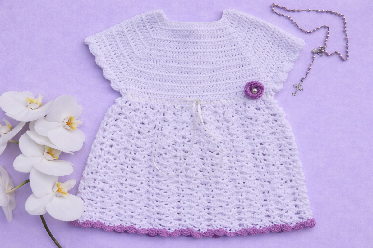 Festliches weißes gehäkeltes Babykleid mit lila Blüte, Orchideen und Perlenkette