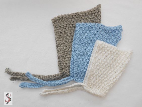 Drei gestrickte Babymützen in Taupe, Hellblau und Cremeweiß mit Bindebändern auf hellem Hintergrund.