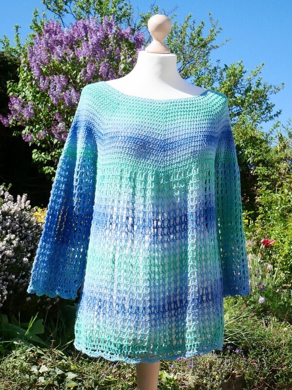 Türkis-blaue Häkel-Tunika mit dichtem Oberteil und offenem Netzmuster auf Schneiderbüste im Garten