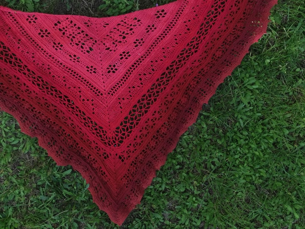 Rotes gehäkeltes Dreieckstuch mit Lochmuster und Farbverlauf, ausgebreitet auf grünem Gras.