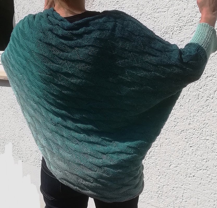 Rückansicht einer Person, die einen gestrickten Poncho mit grünem Farbverlauf und Wellenmuster trägt