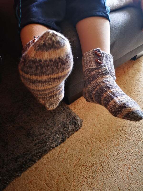 Gestrickte Herrensocken in Braun-, Beige- und Grautönen mit Streifenmuster und Knöpfen am umgeschlagenen Bündchen, getragen beim Sitzen.