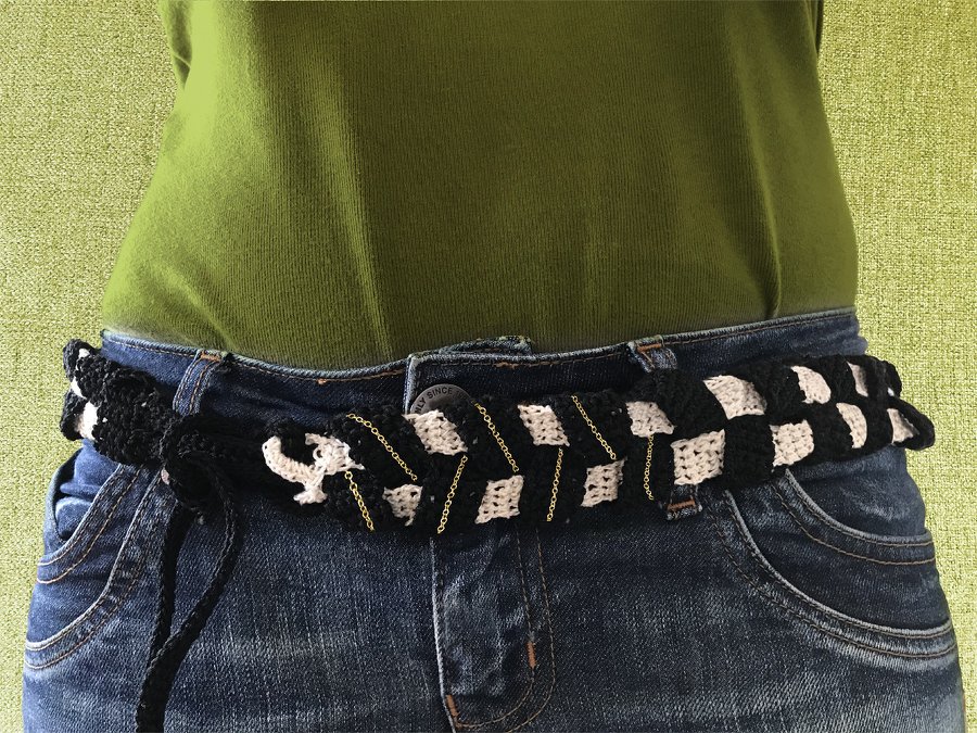 Handgehäkelter Boho-Gürtel in Schwarz-Weiß mit goldfarbenen Ketten und seitlicher Schnürung an einer Jeans