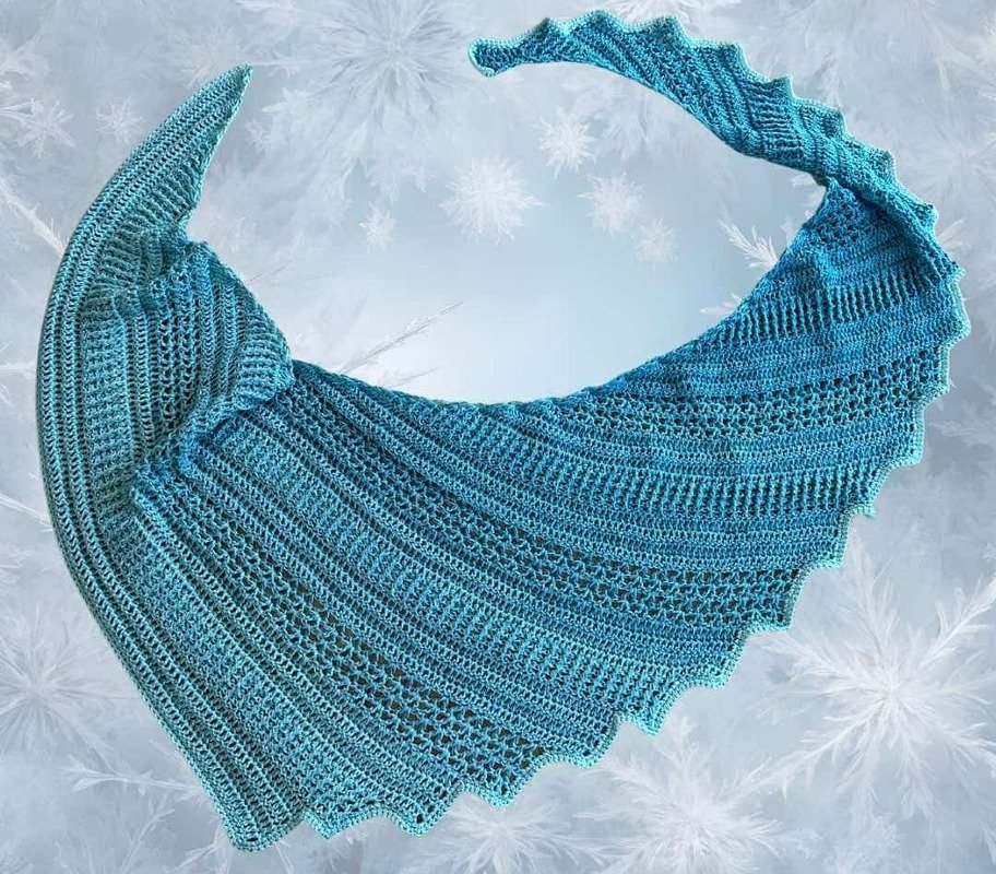 Türkisblauer gehäkelter Drachenschwanz‑Schal mit gewellter Kante vor einem Hintergrund mit Schneeflocken.