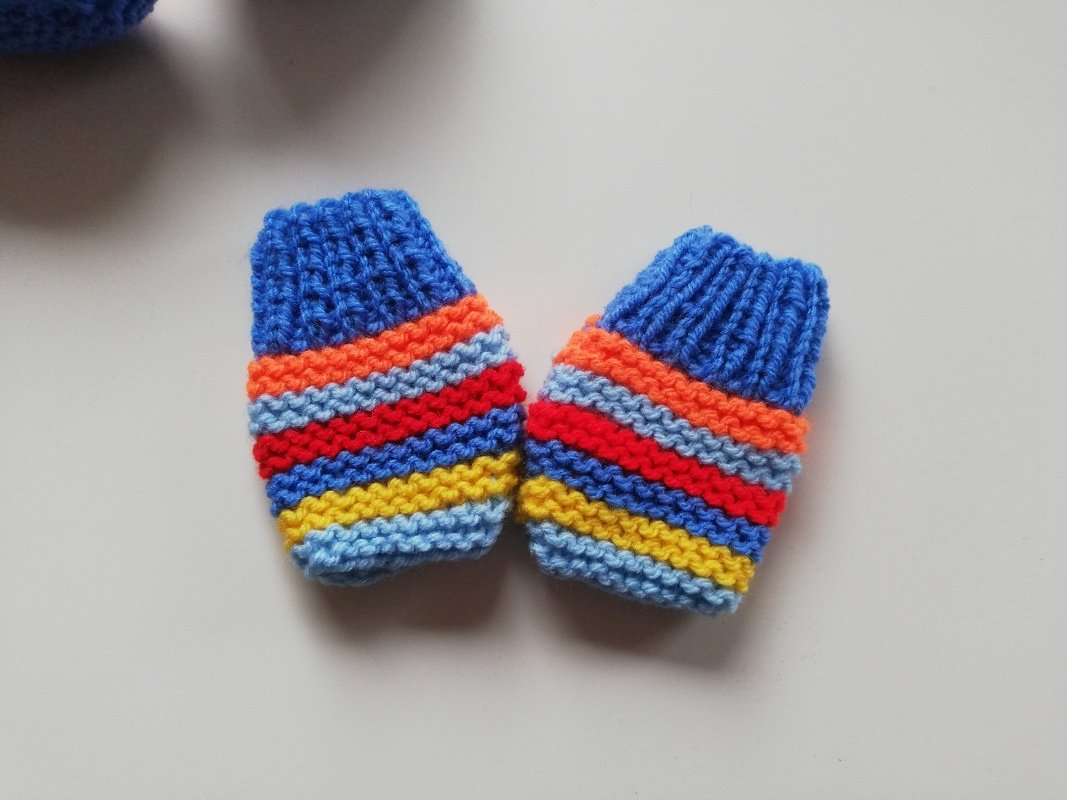 Gestrickte Baby-Fäustlinge mit bunten Querstreifen auf hellem Untergrund