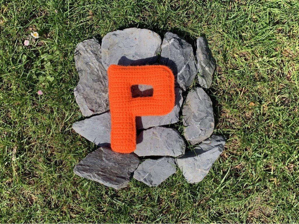 Einfarbiges, dicht gehäkeltes P in Orange auf Schiefersteinen