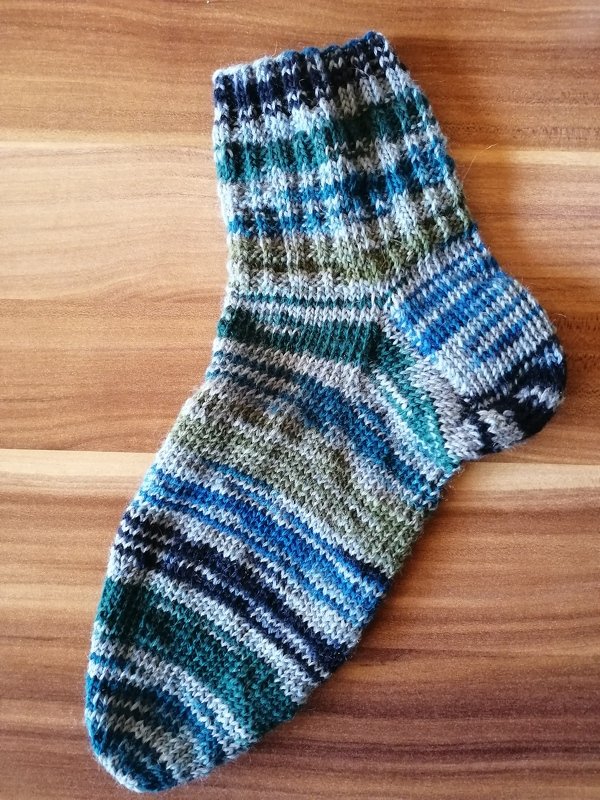 Nahaufnahme einer gestrickten Socke mit Rippenbündchen und mehrfarbigen Streifen auf Holzuntergrund