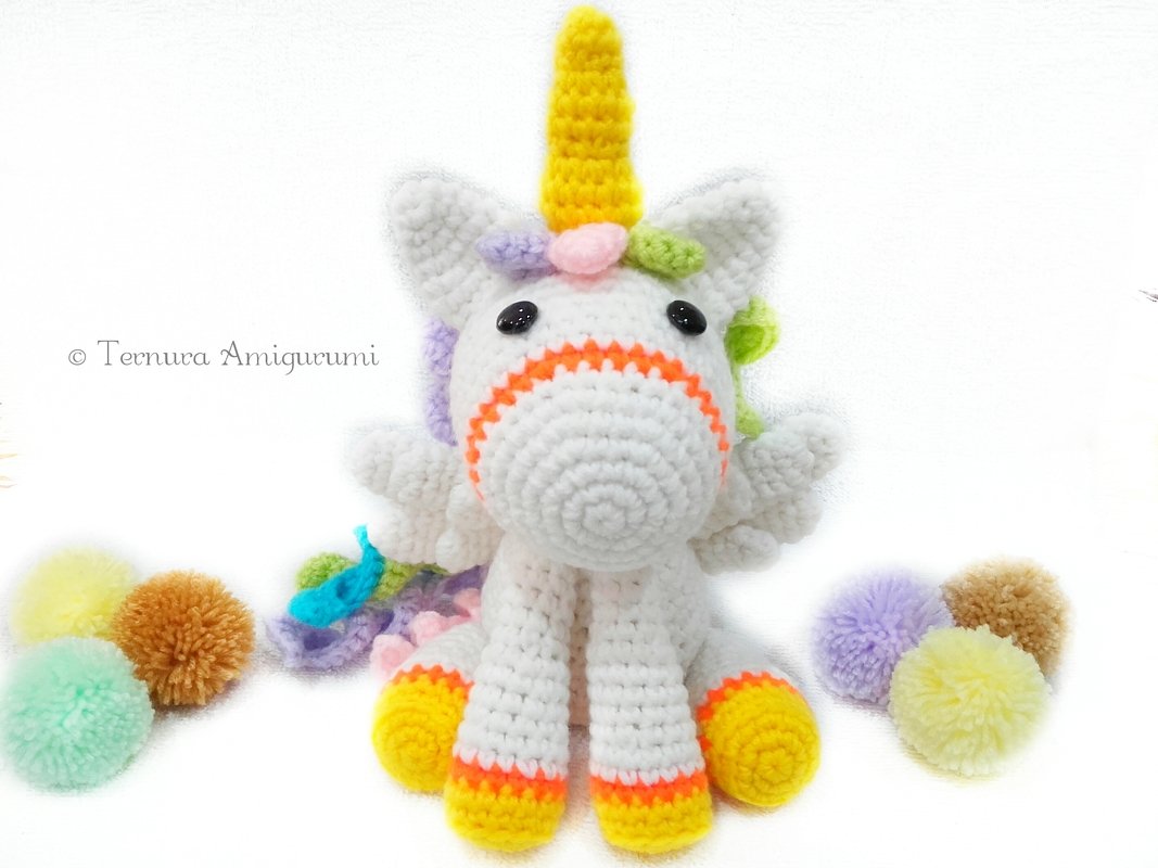 Weißes Amigurumi-Einhorn mit Flügeln, gelbem Horn und pastellfarbener Mähne