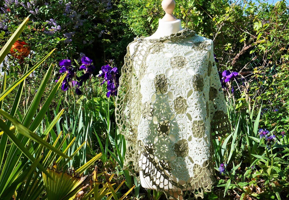 Schaufensterpuppe trägt gehäkeltes Rechtecktuch aus creme- und olivfarbenen Granny-Motiven mit Spitzenrand, im Gartenhintergrund