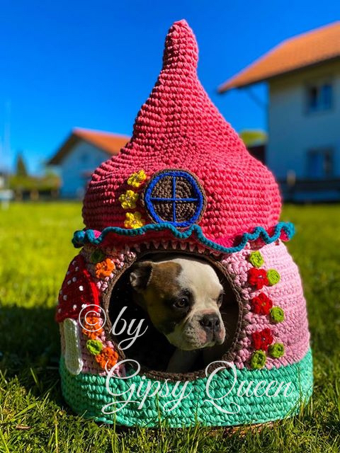 Kleiner Hund sitzt in rundem, buntem gehäkeltem Katzenhaus mit spitzem Dach auf Gras