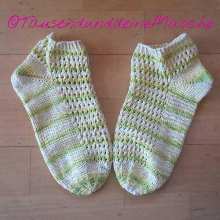 Paar gestrickter knöchelhoher Socken in Weiß und Grün mit Lochmuster, liegend auf Holzboden