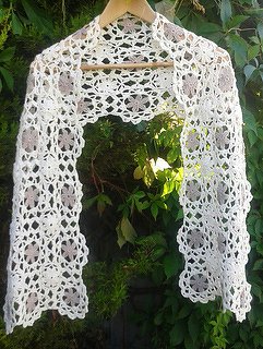 White lacy crochet scarf with floral motifs hanging on a wooden hanger against green foliage