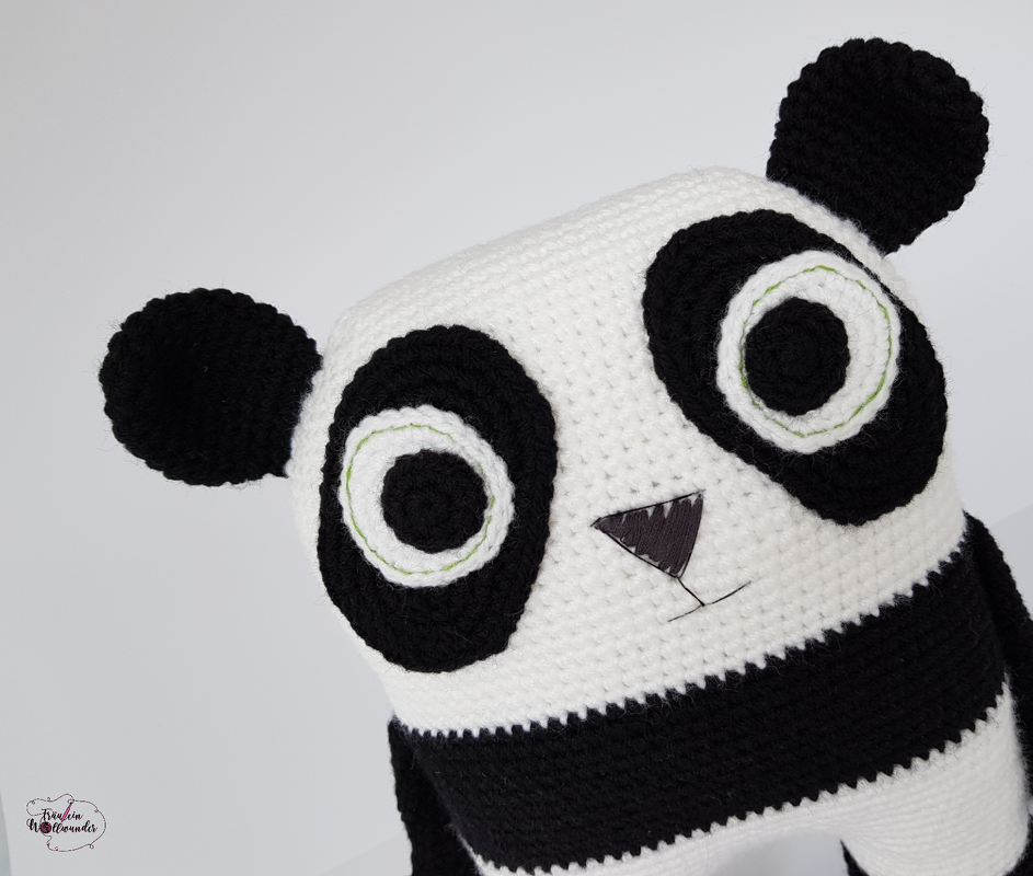 Nahaufnahme eines gehäkelten Panda-Amigurumi mit schwarzen Ohren, weißen Flächen und grünen Augenringen.