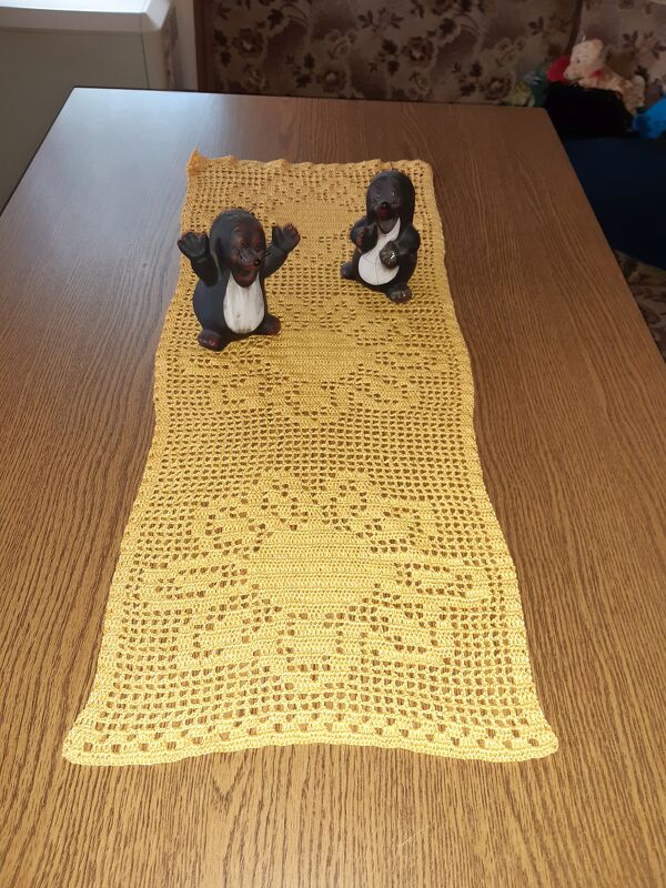 Gelber gehäkelter Tischläufer mit Spitzenmuster auf Holztisch, zwei Maulwurffiguren als Deko