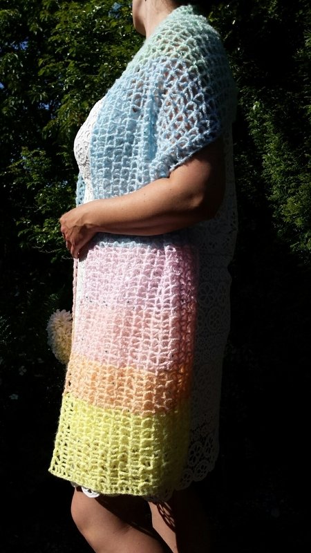 Seitliche Ansicht einer Person mit langer, offen gehäkelter Stola im Pastellverlauf (Blau, Rosa, Gelb) im Netzmuster