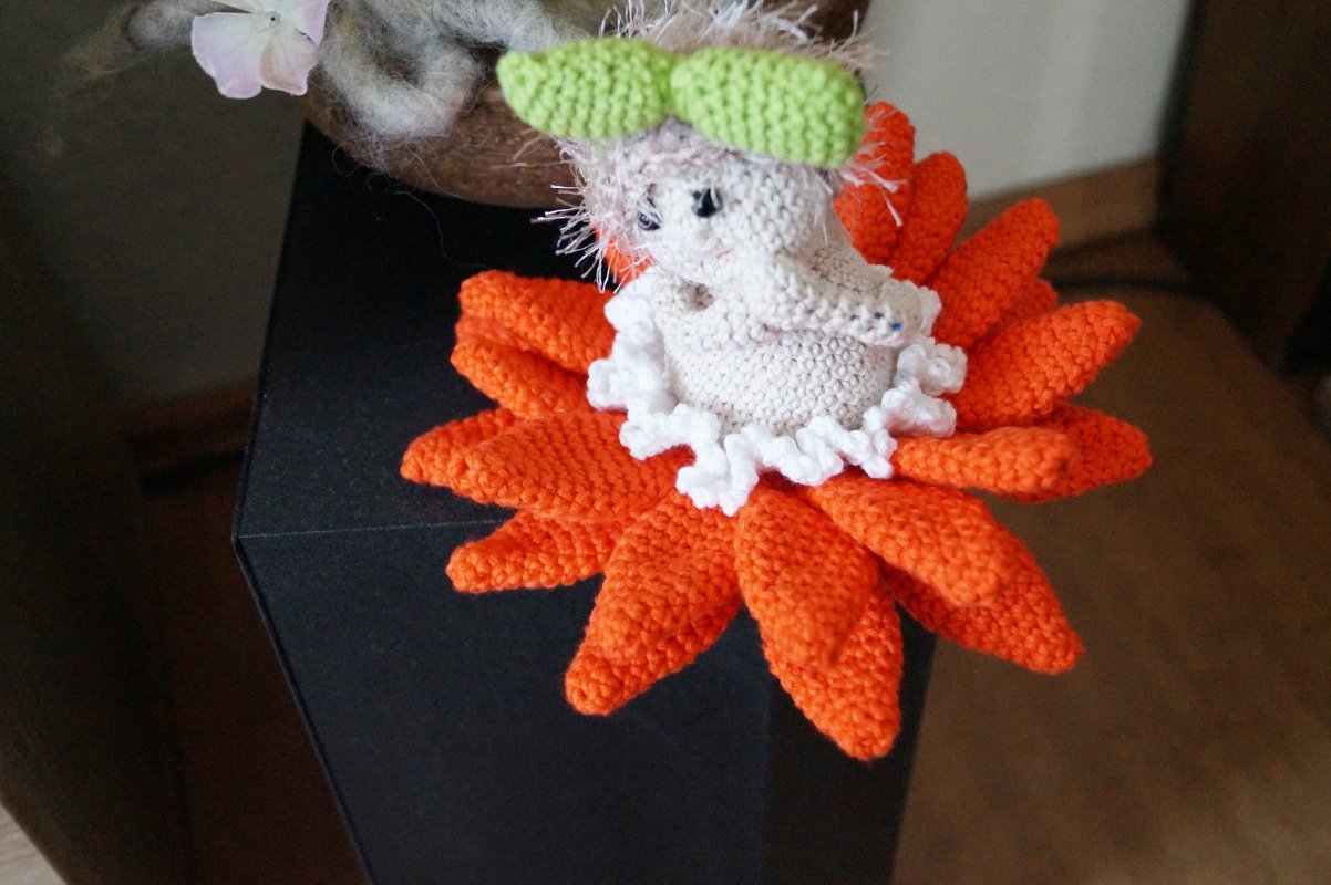 Gehäkelte Schnecke mit grünen Blättern und weißem Rüschenkragen auf orangefarbener Häkelblume