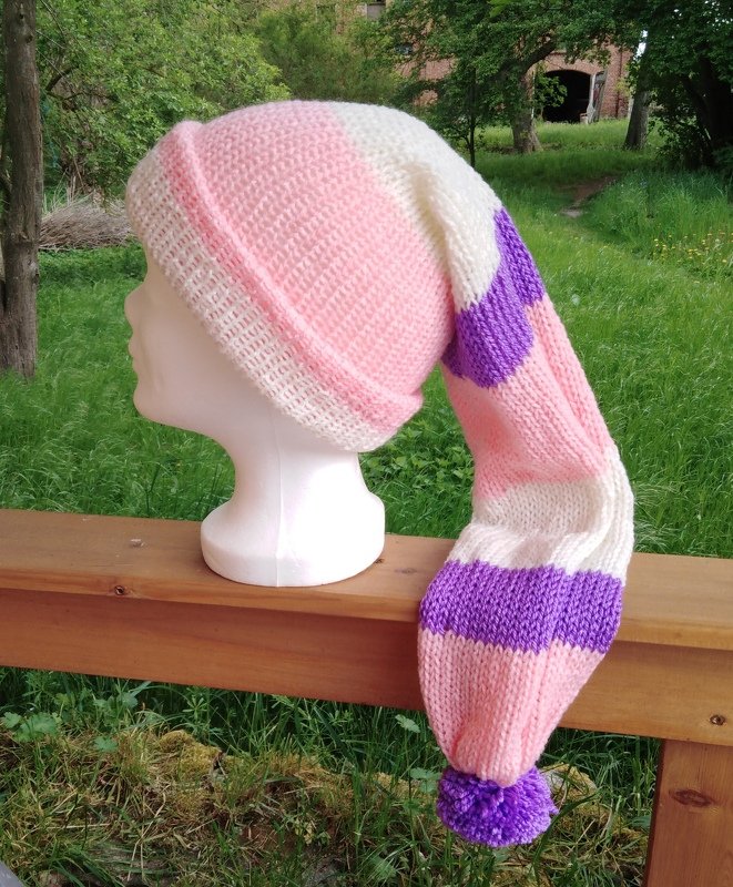 Gestrickte Kindermütze mit langem Zipfel, Rollrand und Bommel in Rosa, Cremeweiß und Violett auf Schaufensterkopf