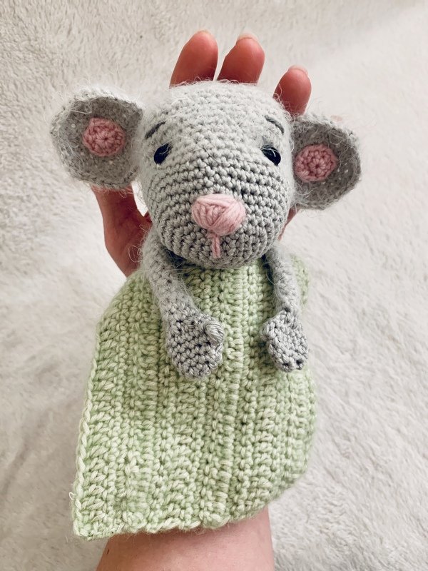 Gehäkelte graue Maus-Handpuppe mit rosa Ohren und Nase und hellgrünem Körper, von einer Hand gehalten vor hellem Hintergrund.