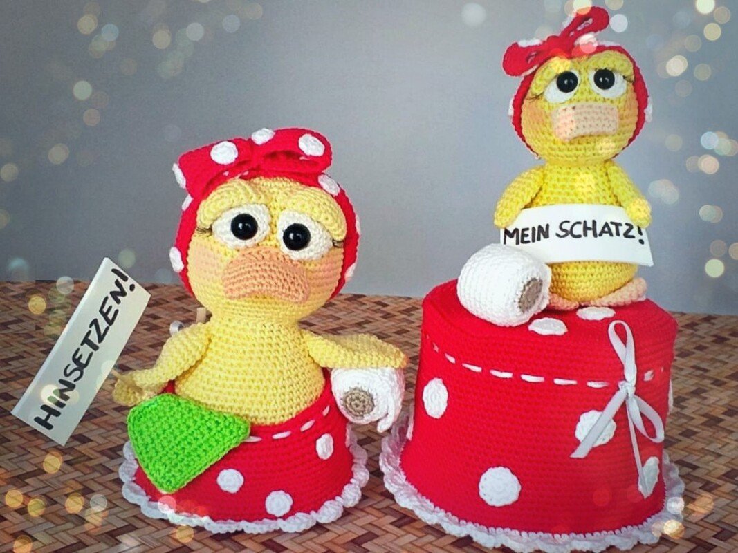 Two yellow crocheted amigurumi chicks in red polka-dot bonnets and skirts holding handwritten German signs