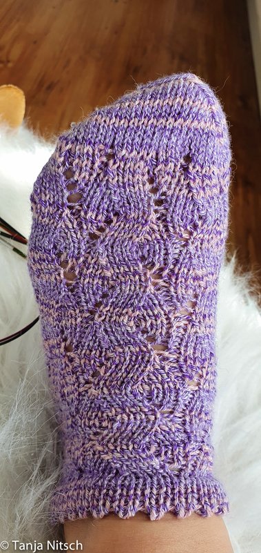 Violett-rosa melierte, handgestrickte Socke mit Lochmuster und Wellenrand auf einem Fuß