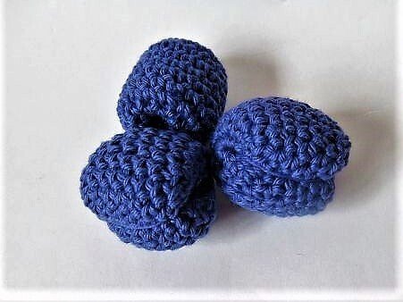 Drei dunkelblaue, gehäkelte Blaubeeren auf hellem Hintergrund