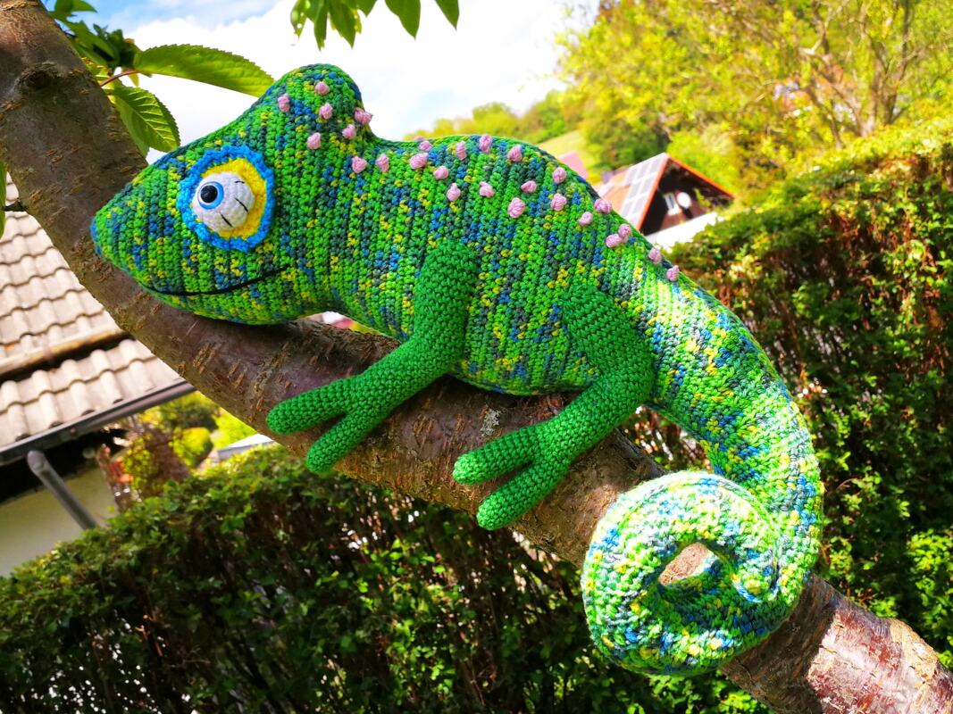 Grünes gehäkeltes Chamäleon-Amigurumi mit spiralförmigem Schwanz auf einem Ast
