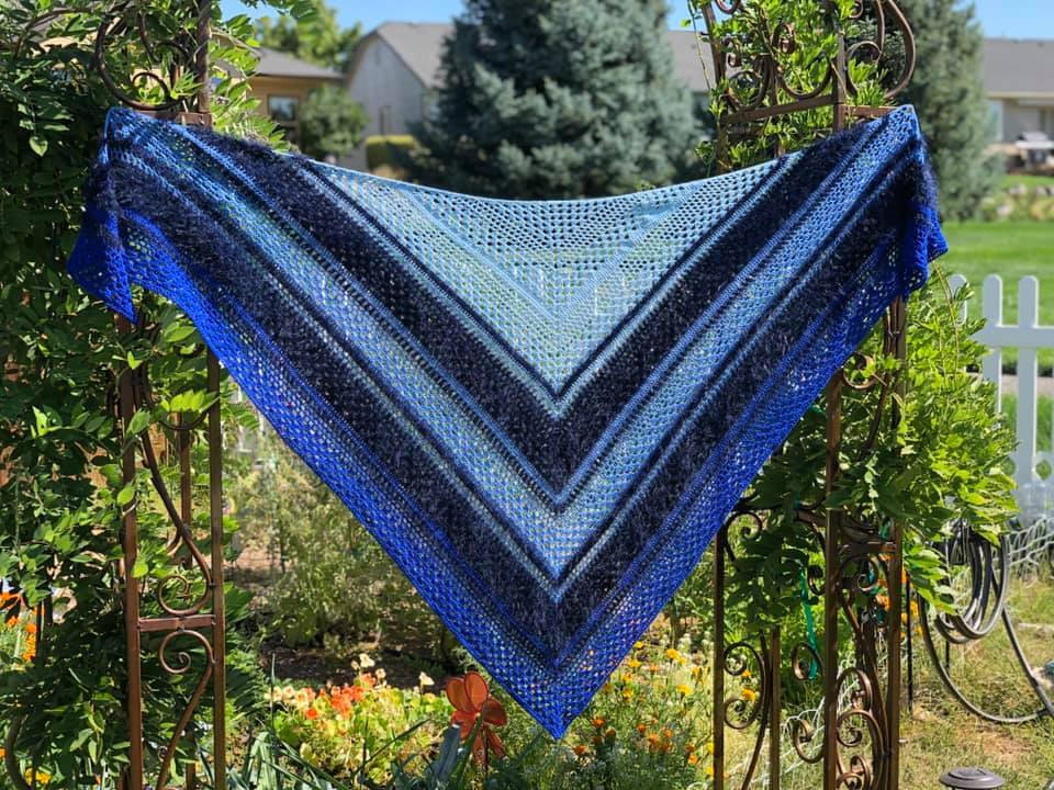 Triangle crochet shawl in blue gradient with lace mesh, draped on a metal garden arbor