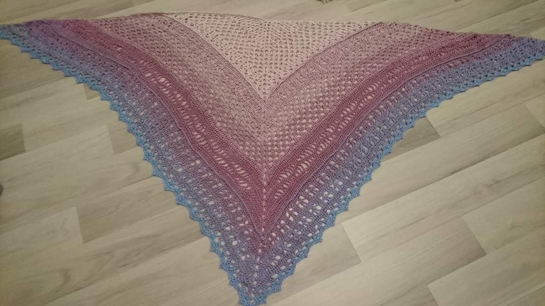 Gehäkeltes Dreieckstuch in Pastellfarben mit Farbverlauf von Rosa zu Blau, liegend auf hellem Holzboden.