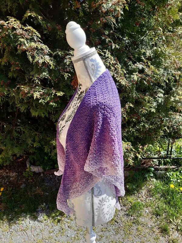 Schneiderpuppe mit gehäkelter Stola in Lila-zu-Hellrosa-Farbverlauf vor Hecke