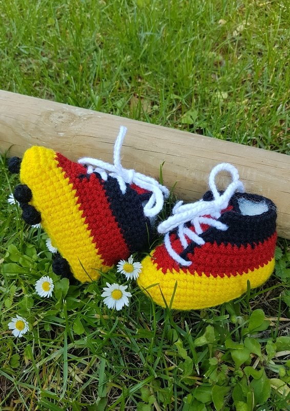 Gehäkelte Babyschnürer in Schwarz, Rot und Gelb mit weißen Schnürsenkeln auf Gras