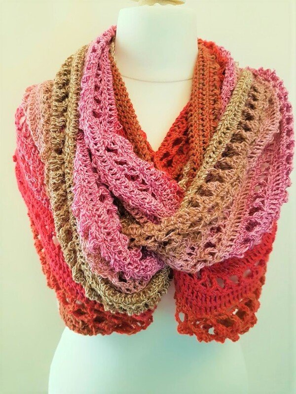 Gehäkelter Loop-Schal in Rosa, Beige und Rot-Orange mit offenem Muster auf einer Schaufensterpuppe.