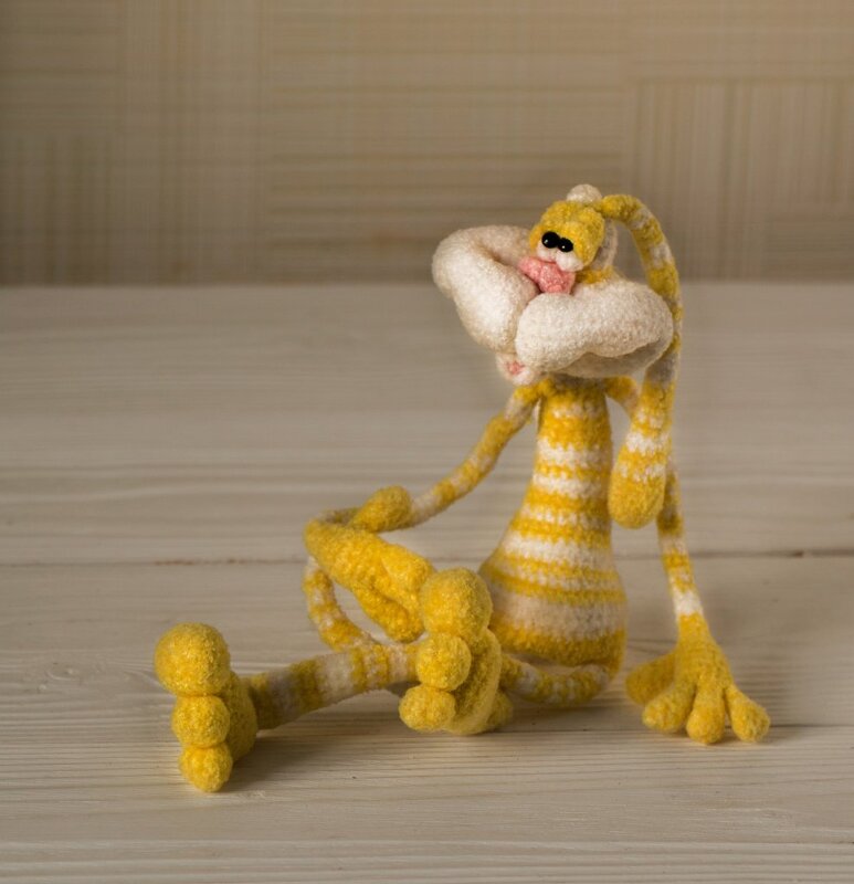 Gehäkelter gelb-weiß gestreifter Osterhase mit langen Ohren sitzt auf einer hellen Holzoberfläche.