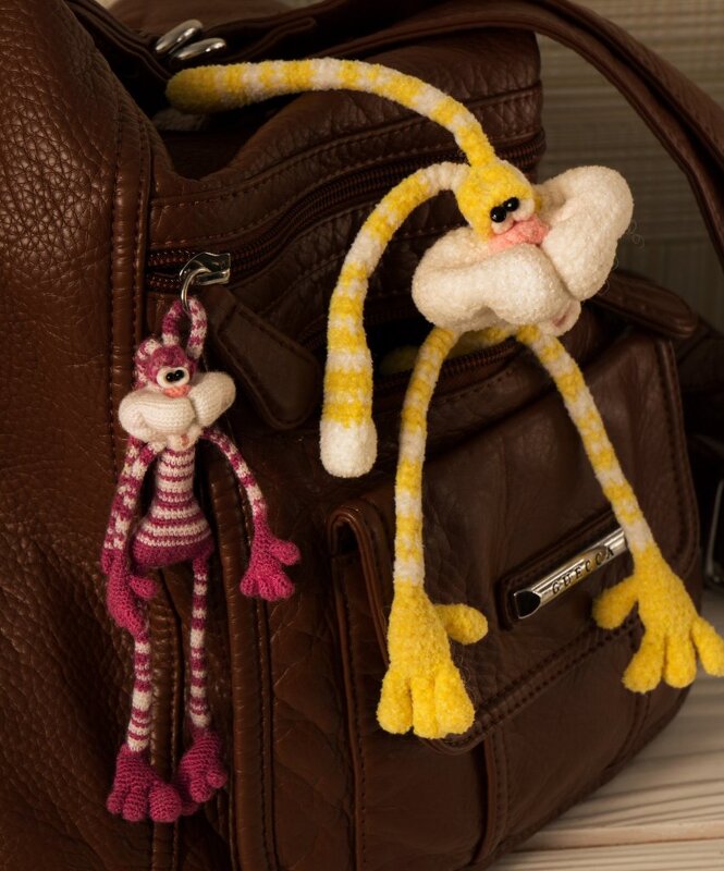 Zwei gehäkelte Hasen-Anhänger in Rosa-Weiß und Gelb-Weiß an einer braunen Handtasche