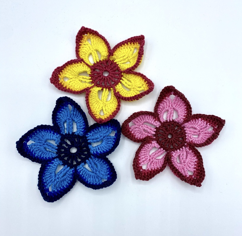 Drei schnell gehäkelte fünfblättrige Blumenapplikationen in Gelb, Blau und Rosa