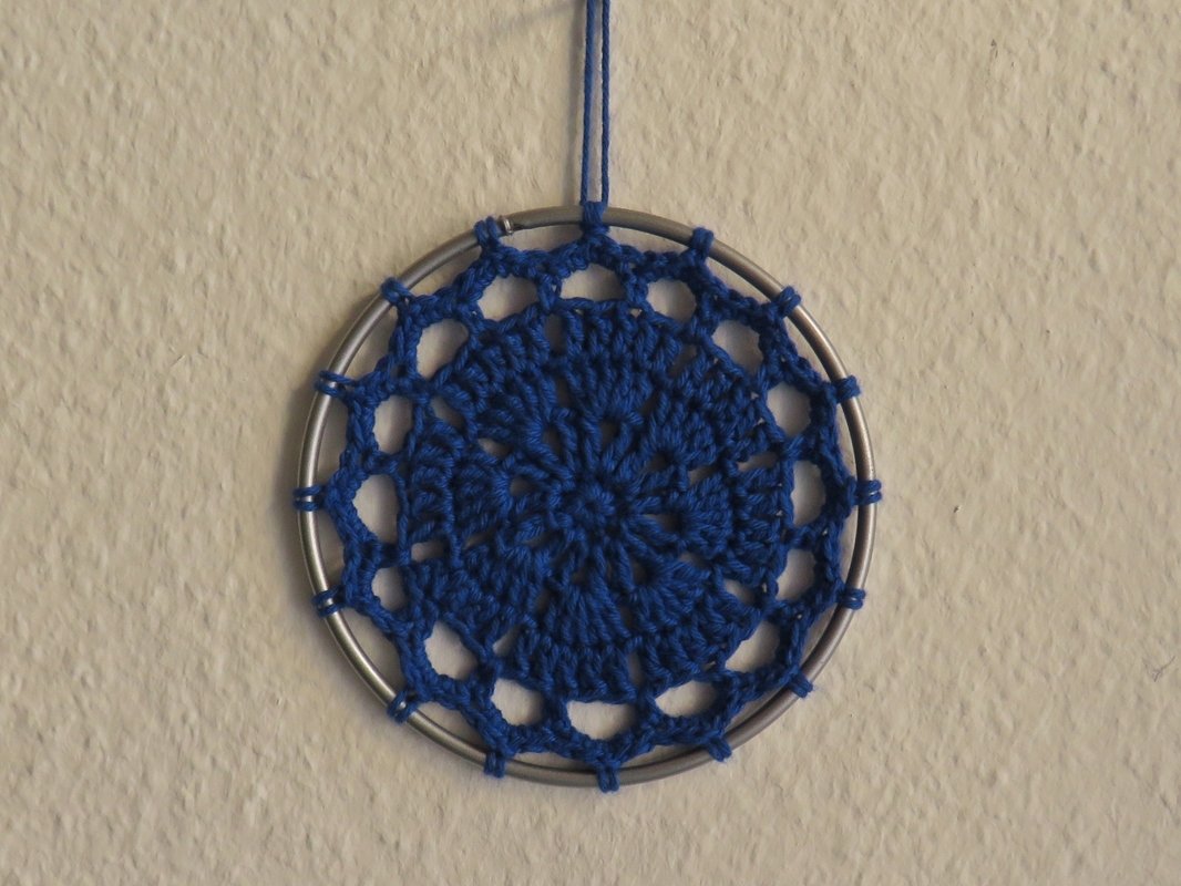Blauer gehäkelter Traumfänger mit Metallring an heller Wand