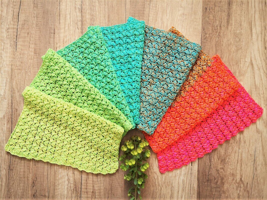 Fünf gehäkelte Rechtecktücher in Grün, Türkis, Orange und Pink auf Holzuntergrund