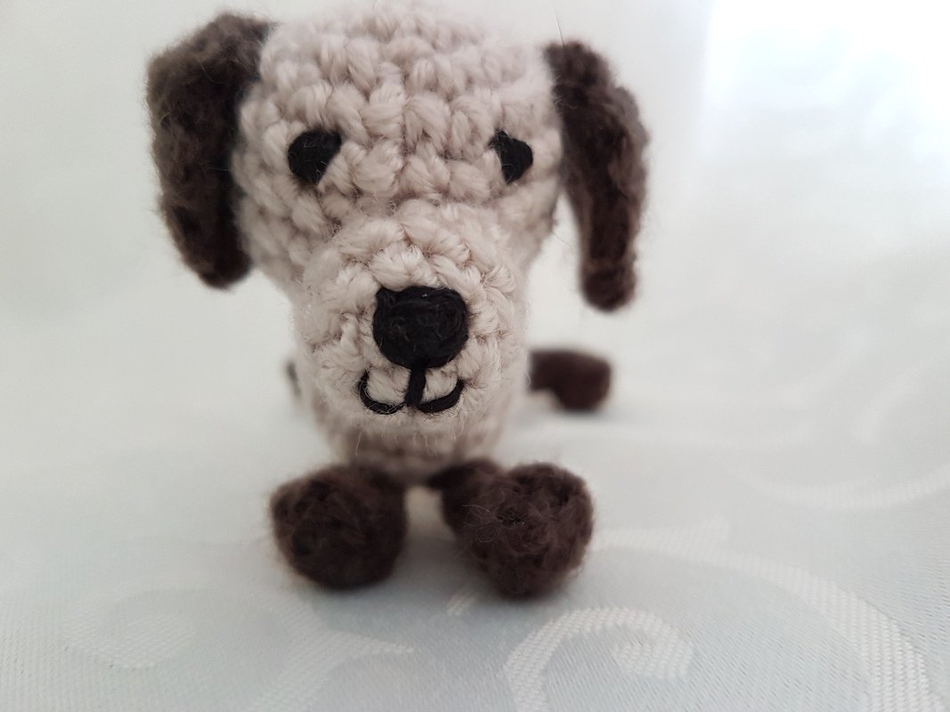 Nahaufnahme eines kleinen gehäkelten Hundeamigurumi mit sichtbaren Maschen und gestickter Nase