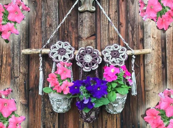 Häkel-Blumenampel am Ast mit pinken und violetten Blüten vor Holzlattenwand