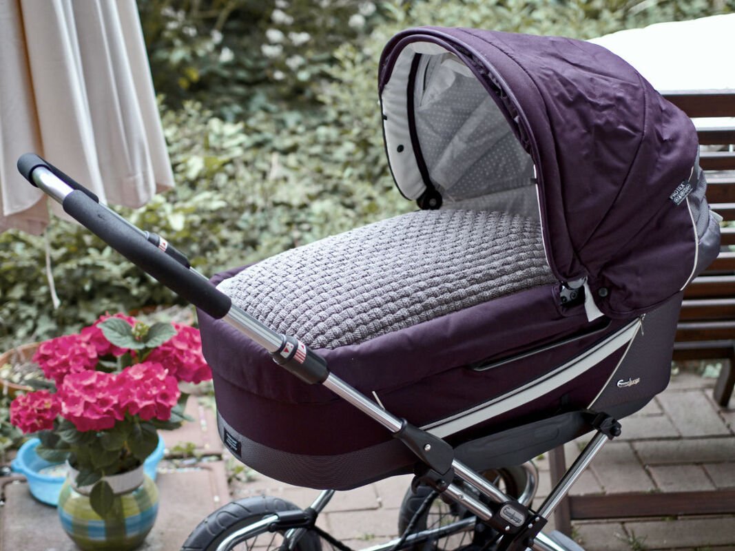 Nahaufnahme eines Kinderwagens mit einer elegant hellgrauen, gestrickten Decke als Geschenkidee zur Geburt
