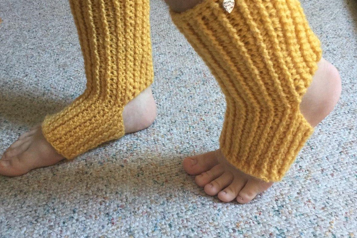 Gelbe gehäkelte Beinstulpen mit Fußschlaufe an nackten Füßen auf Teppich