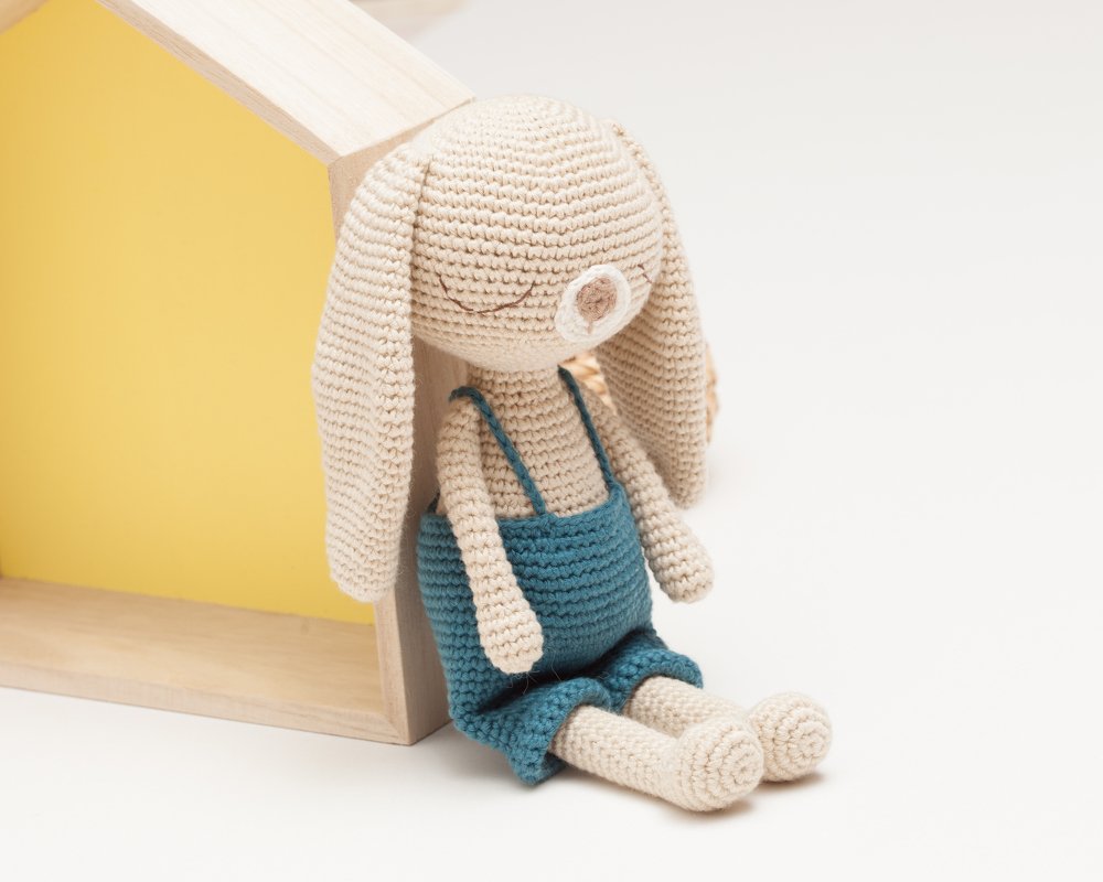 Gehäkelter beige Amigurumi-Hase mit blauer Latzhose, sitzend, lange Ohren