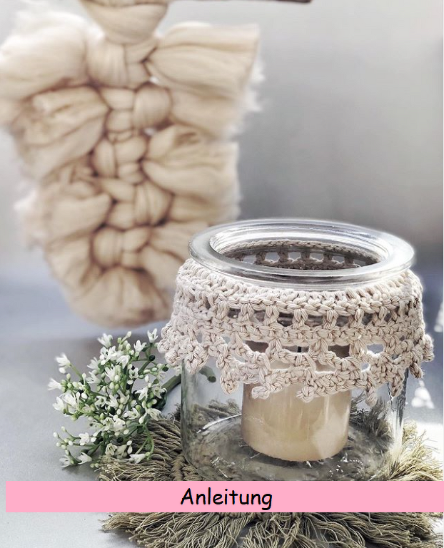 Glaswindlicht mit hellbeiger Häkelspitze und Kerze, dekoriert mit kleinen weißen Blüten und Makramee‑Elementen